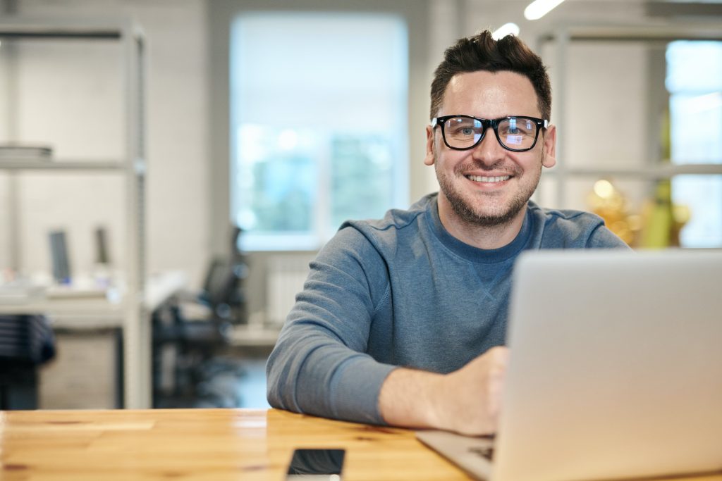 smiling man with glasses in front of laptop