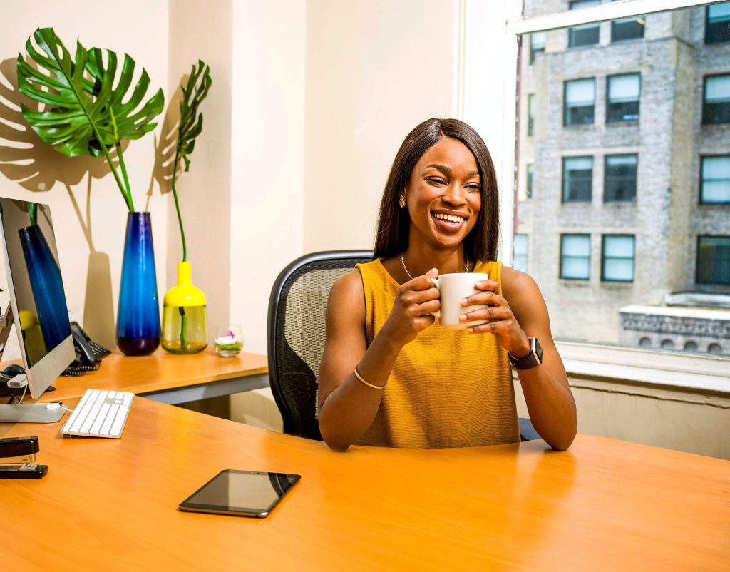 smiling woman sitting behind desk holding a mug