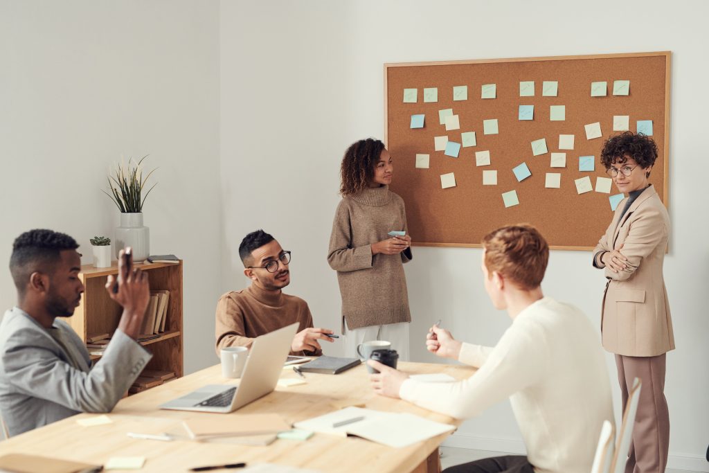 People in business meeting standing and sitting around conference table working on project.