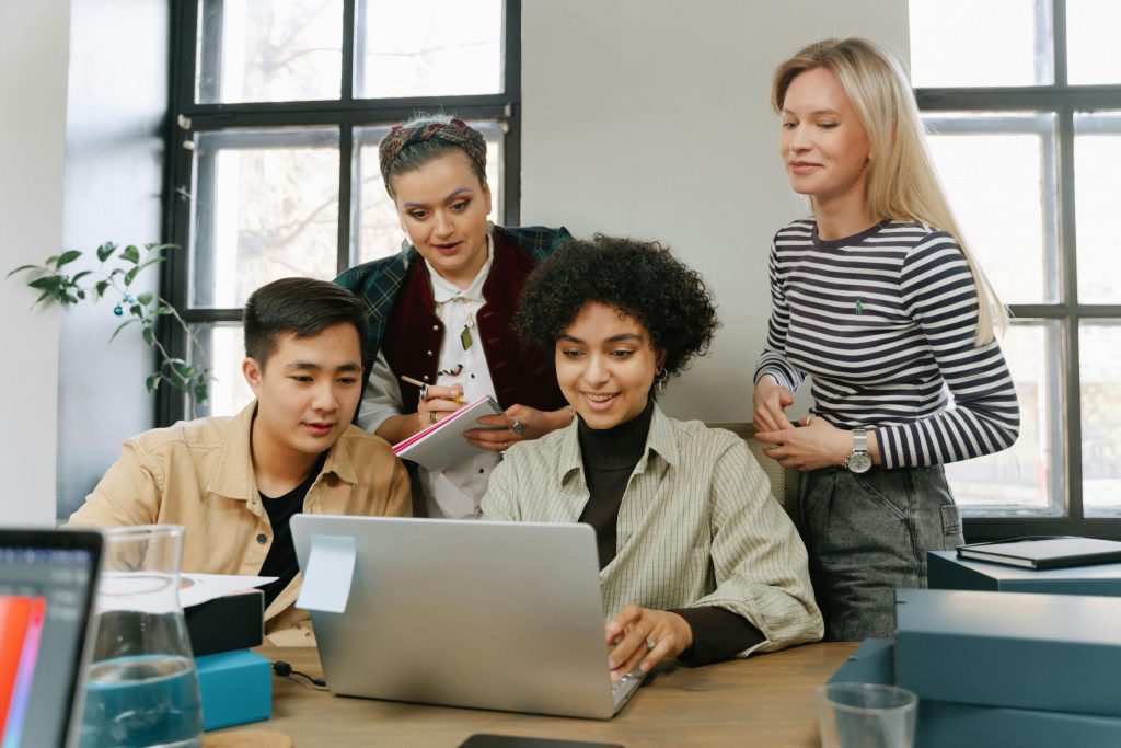 four young people gathered around a laptop in an office setting