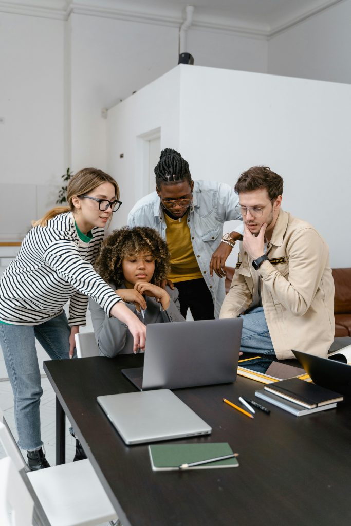 four young people gathered around a laptop pointing and smiling