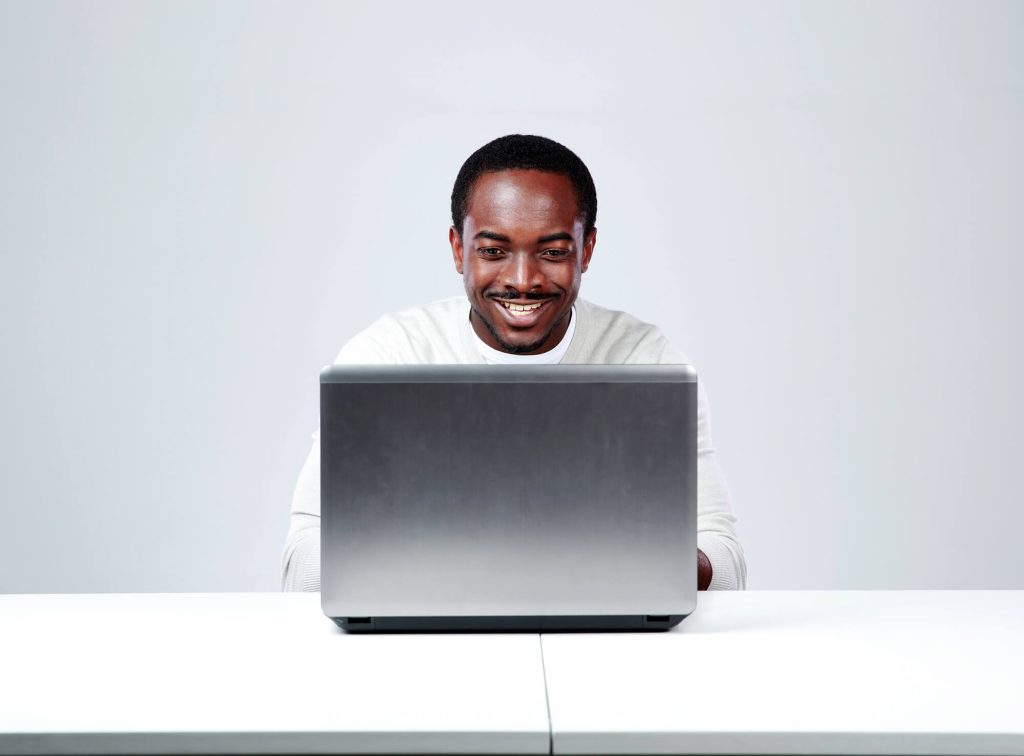 smiling man sitting at a desk using a laptop computer