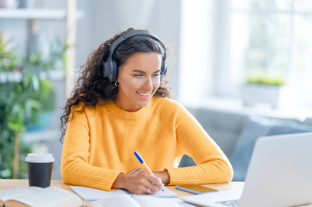 woman with headphones on working on laptop and writing